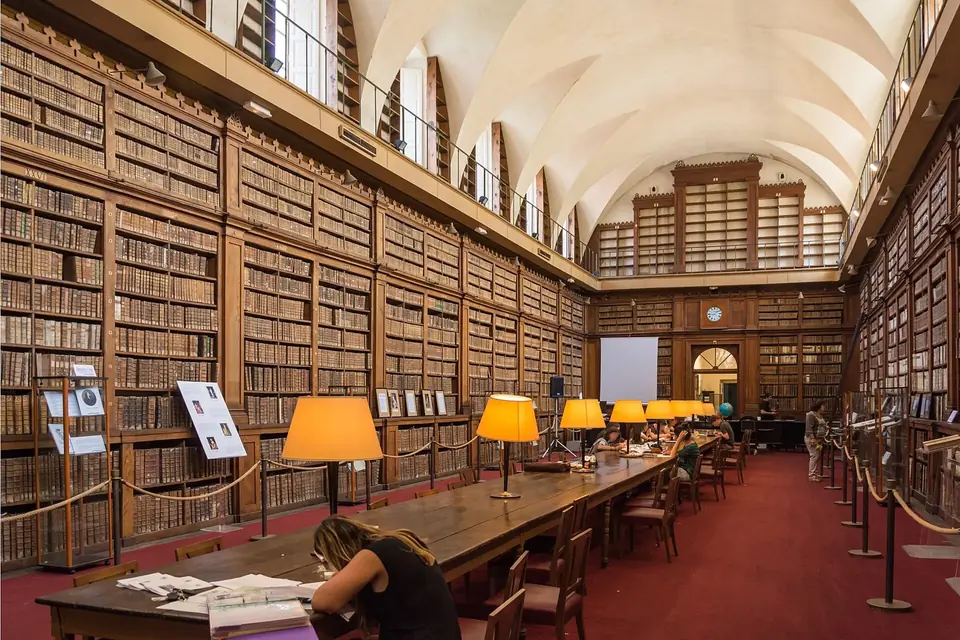 Grande salle de lecture voûtée de la bibliothèque du palais Fesch, rayonnages de livres anciens en noyer sur deux niveaux et longue table centrale avec lampes