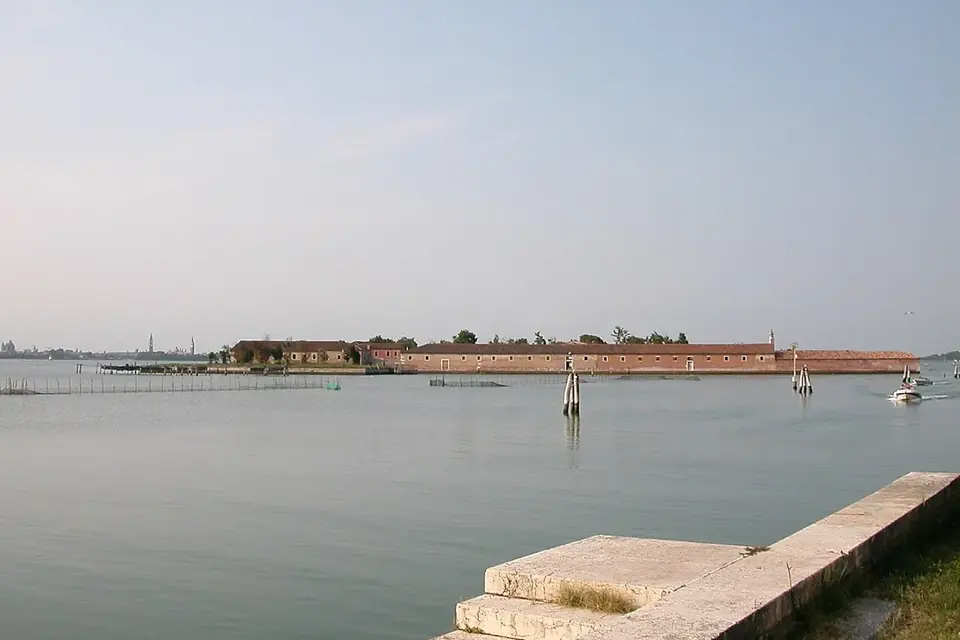 L'île du Lazzaretto Vecchio dans la lagune de Venise, longue ligne de bâtiments bas au ras de l'eau sous un ciel voilé