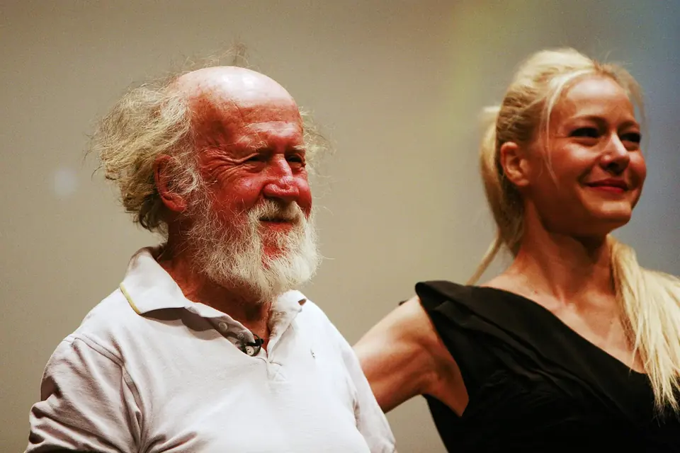 Hubert Reeves, barbe blanche, souriant sur une scène aux côtés d'une interprète vêtue de noir
